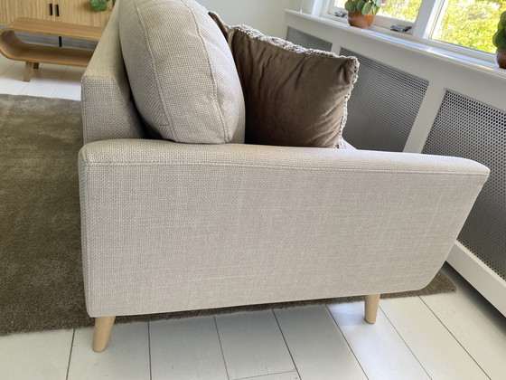 Image 1 of Elegante sofá de 3 plazas con tapicería de tela beige y patas de madera.