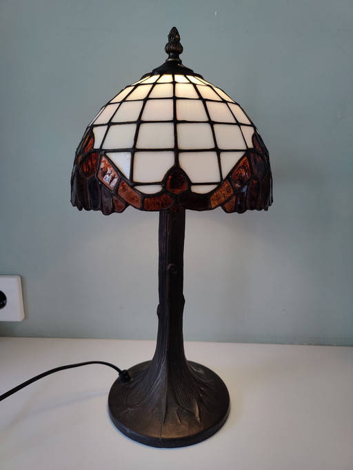 Lámpara de mesa estilo Tiffany con pantalla de vidrieras y base de bronce.