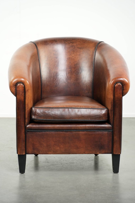 Mooie en karaktervolle schapenleren clubfauteuil met mooie diepe warme kleuren, zwarte biezen en een comfortabele zit