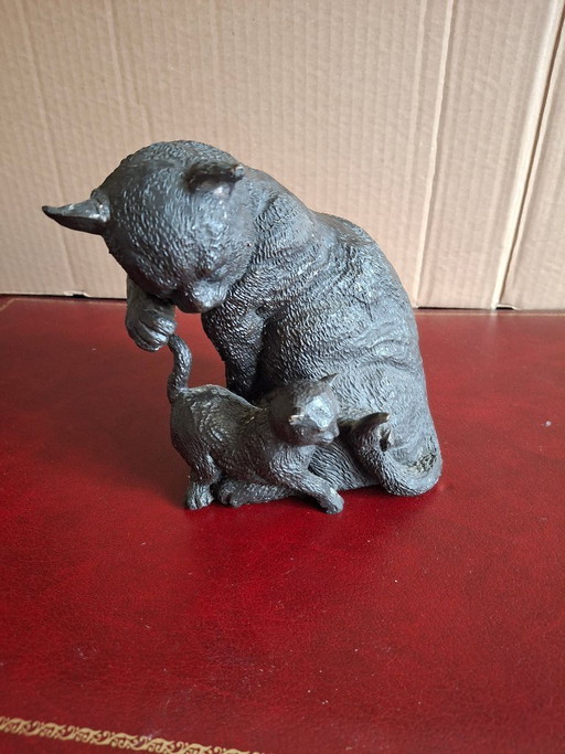 Escultura de bronce de un gatito jugando con la cola de un gato.