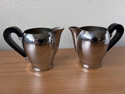 2 vintage Carlo Alessi stainless steel milk jugs with rounded tops and Bakelite handles.