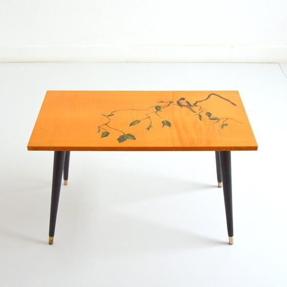 Image 1 of Pretty coffee table from the 50s/60s.  Decorated with a bird on a branch.  Black brass-finish tapered legs.  L 80/ W 40/ H 51
