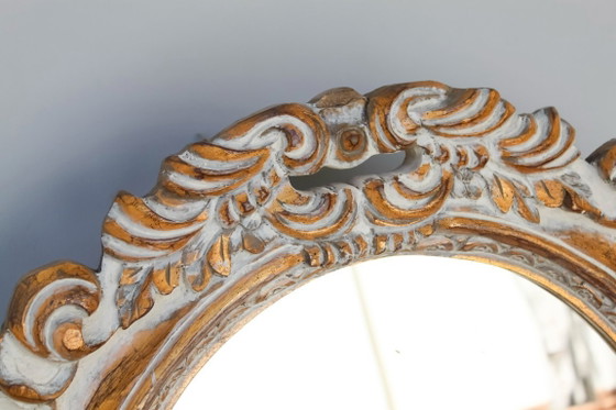 Image 1 of Oval mirror, gilded and carved from wood. Decorated and distressed with scrolls and leaves. Exclusively handmade by artisans.
