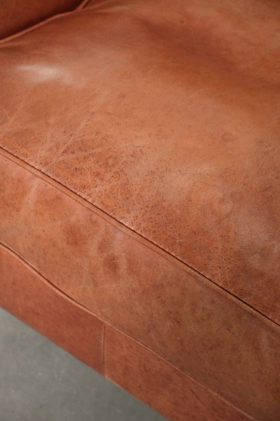 Image 1 of Fauteuil à oreilles en cuir de vachette couleur cognac clair, avec passepoil assorti et un style anglais plein de caractère.