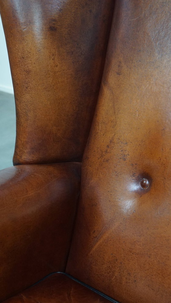 Image 1 of Schapenleren oorfauteuil met een warme kleurstelling en een afwerking met siernagels en zwarte biezen