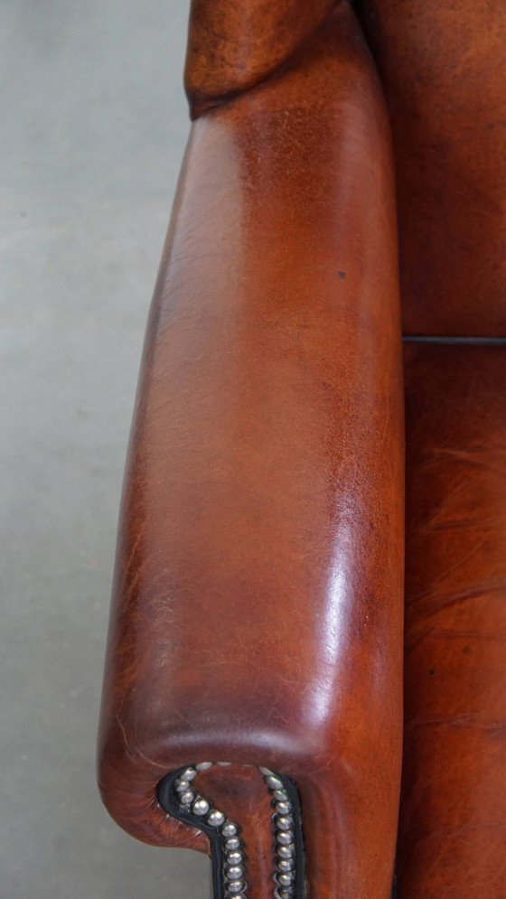 Image 1 of Schapenleren oorfauteuil met een warme kleurstelling en een afwerking met siernagels en zwarte biezen