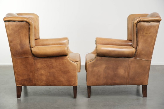Image 1 of Dos hermosos sillones orejeros de piel de vaca clara con un estilo inglés atemporal y gran comodidad.