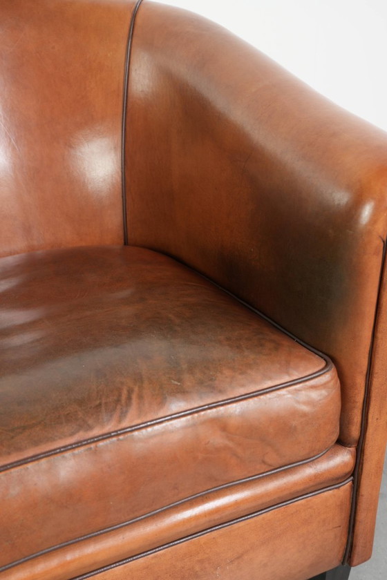 Image 1 of Vintage schapenleren clubfauteuil met een warme kleurstelling en afgewerkt met zwarte biezen