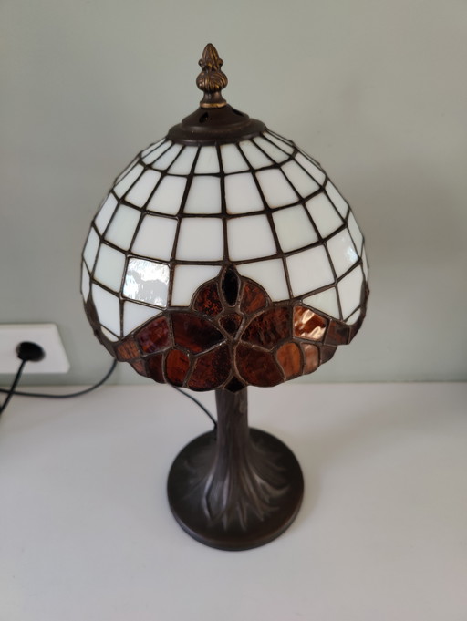 Lámpara de mesa estilo Tiffany con pantalla de vidrieras y base de bronce.