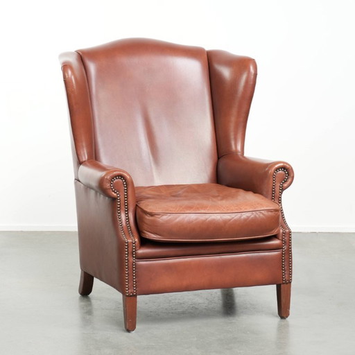 Cómodo sillón orejero de piel de vacuno color coñac al estilo inglés.