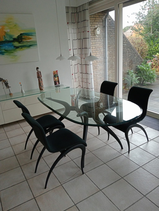Mesa de comedor ovalada de cristal con 4 sillas negras a juego.