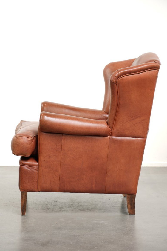 Image 1 of Fauteuil à oreilles en cuir de vachette couleur cognac clair, avec passepoil assorti et un style anglais plein de caractère.