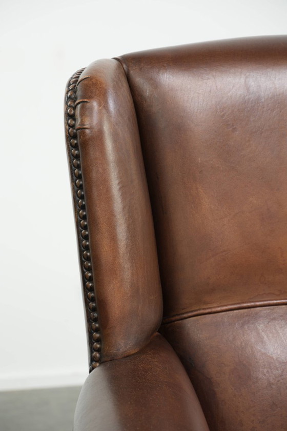 Image 1 of Precioso sillón orejero de piel de oveja marrón oscuro con un aspecto atemporal en un tamaño sutil.