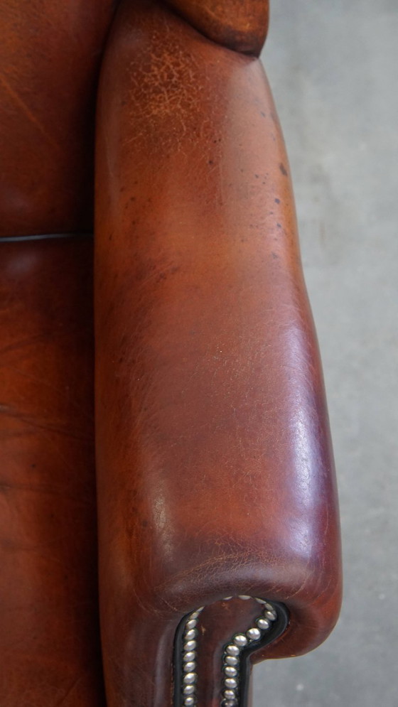 Image 1 of Schapenleren oorfauteuil met een warme kleurstelling en een afwerking met siernagels en zwarte biezen