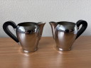 2 vintage Carlo Alessi stainless steel milk jugs with rounded tops and Bakelite handles.
