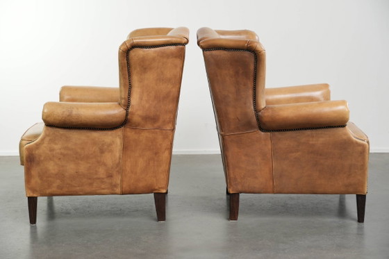 Image 1 of Dos hermosos sillones orejeros de piel de vaca clara con un estilo inglés atemporal y gran comodidad.