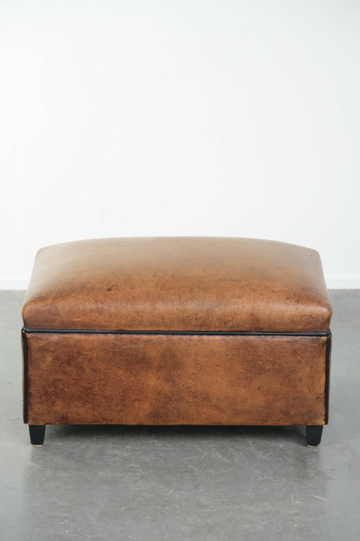 Characterful sheepskin footstool/ottoman with a beautiful patina and finished with black piping.