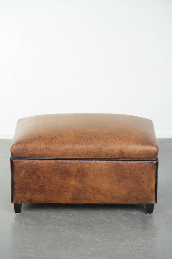 Image 1 of Characterful sheepskin footstool/ottoman with a beautiful patina and finished with black piping.