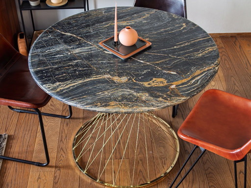 Lujosa mesa de comedor redonda con tablero de mármol negro y base dorada.