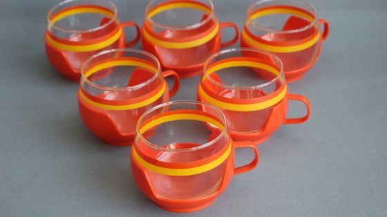 Image 1 of 12 vintage glazen theekopjes met geel-oranje strepen en oranje plastic houders.