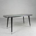 Vintage salontafel met glazen blad en schuine, taps toelopende poten. jaren 50