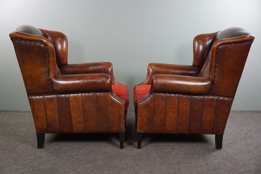 Set of two sheep leather wing chairs with red corduroy seat cushions